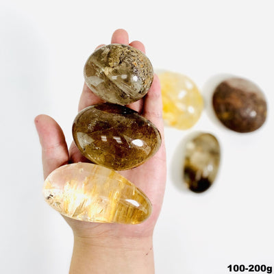 Lodolite tumbled stone assortment on a white background with three held in a man's hand