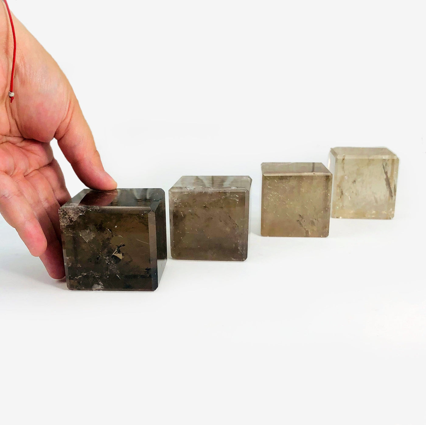 four smokey quartz cubes in a diagonal line with a hand holding the first one for size reference