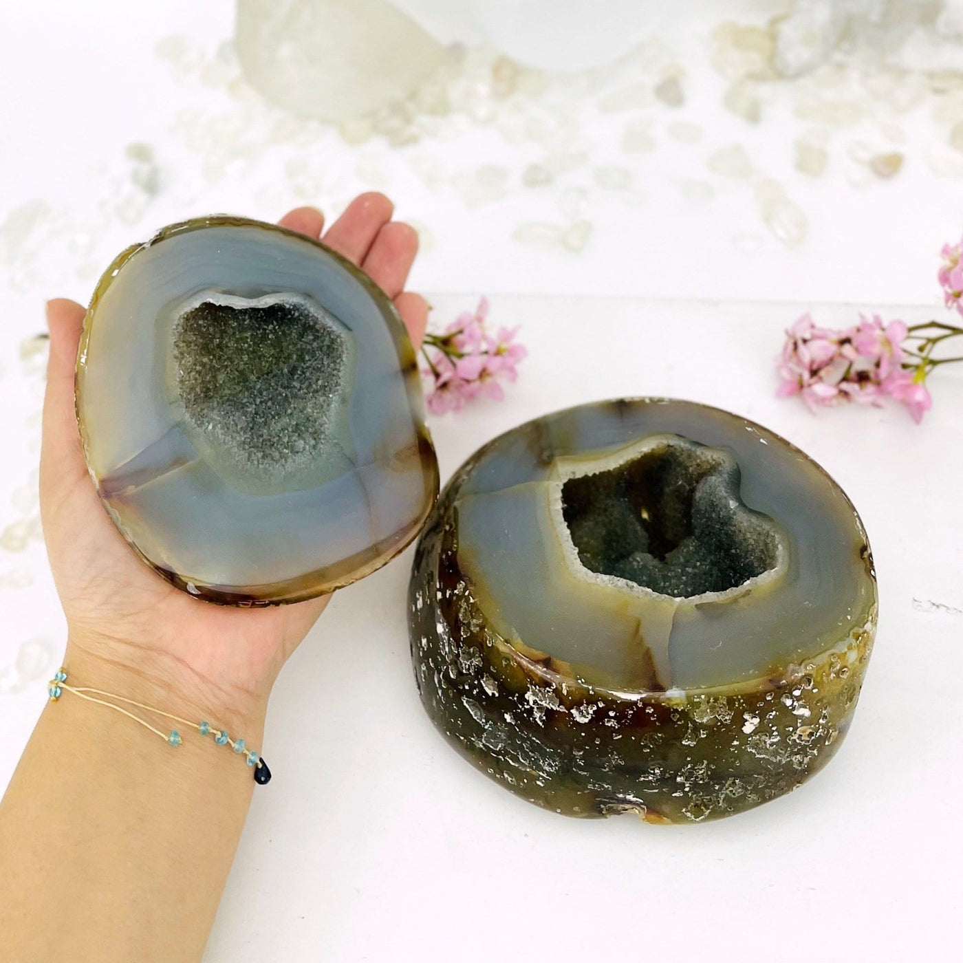 Agate geode box open displaying the pattern and druzy, one half of the geode is in a hand. Flowers in the background.