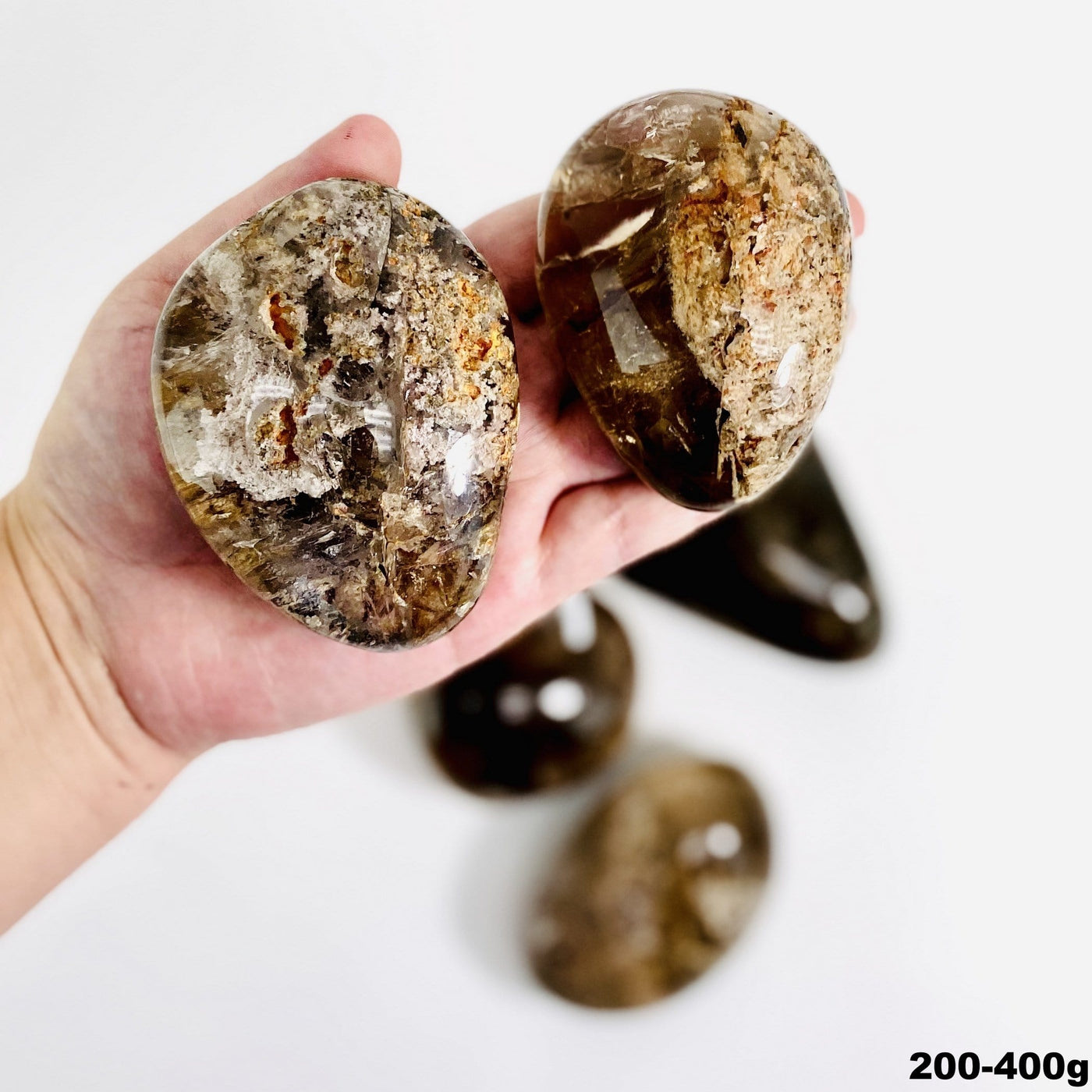 Lodolite tumbled stone assortment on a white background with two held in a man's hand