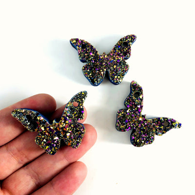 hand holding up butterfly druzy pendant with others in the background