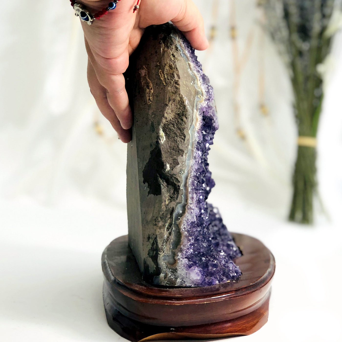 hand showing side view of Amethyst Cluster on Wooden Base with decorations in the background