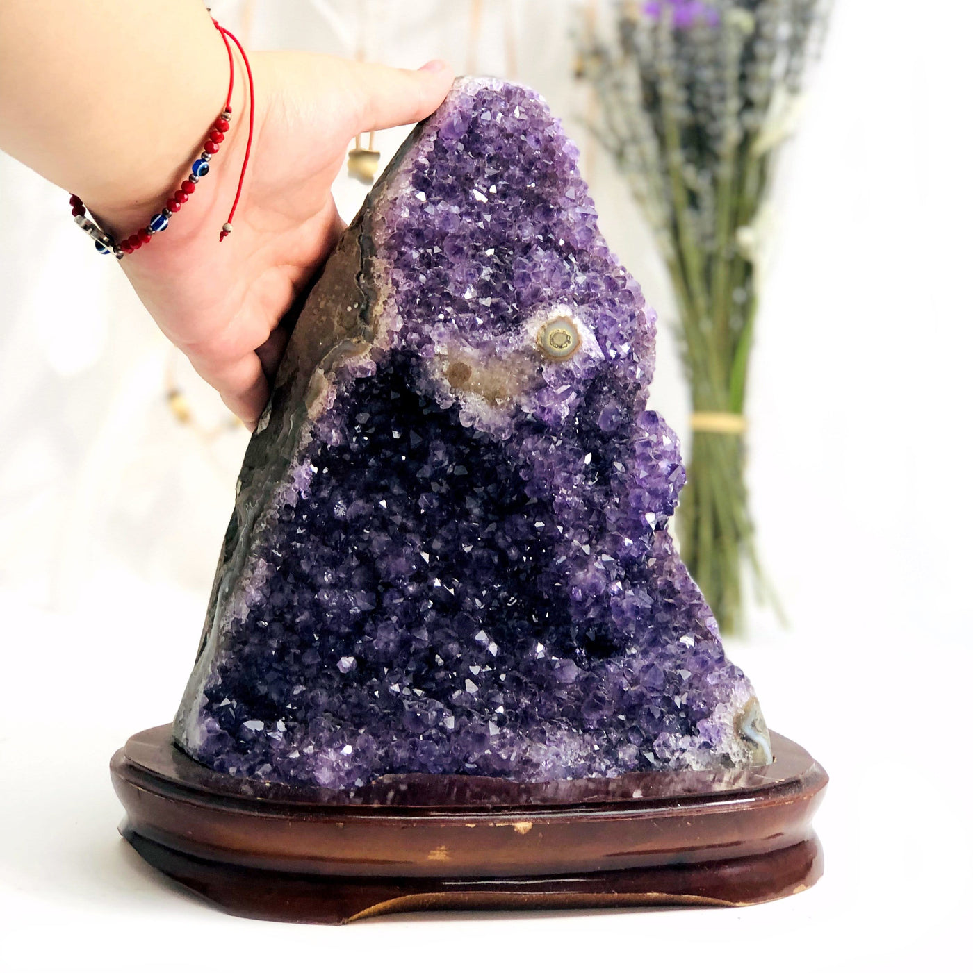 hand behind Amethyst Cluster on Wooden Base with decorations in the background