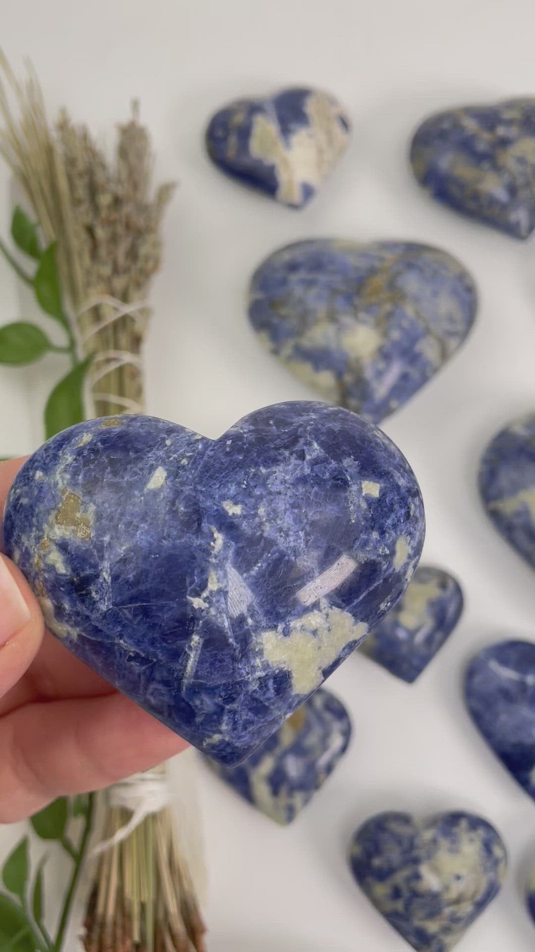 video of one sodalite heart shaped stone in hand that pans to many different sodalite heart shaped stone weights on display