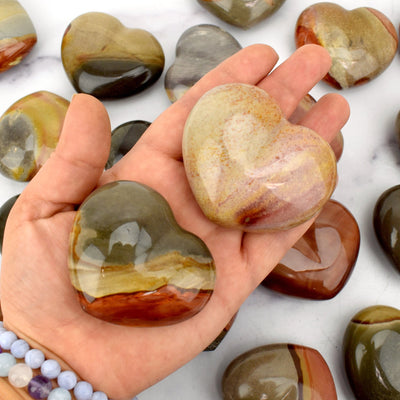 Hand holding 2 Polychrome Jasper Polished Hearts For Size Reference 