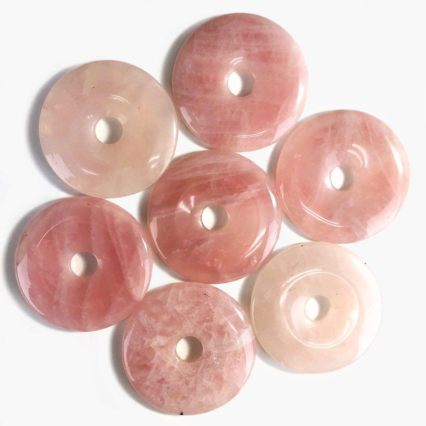 7 rose quartz donut shaped polished stones on white background