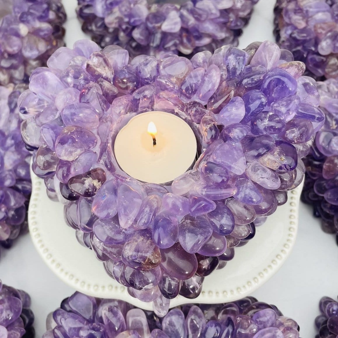 up close shot of amethyst tumbled stone heart candle holder with candle lit up inside of it 