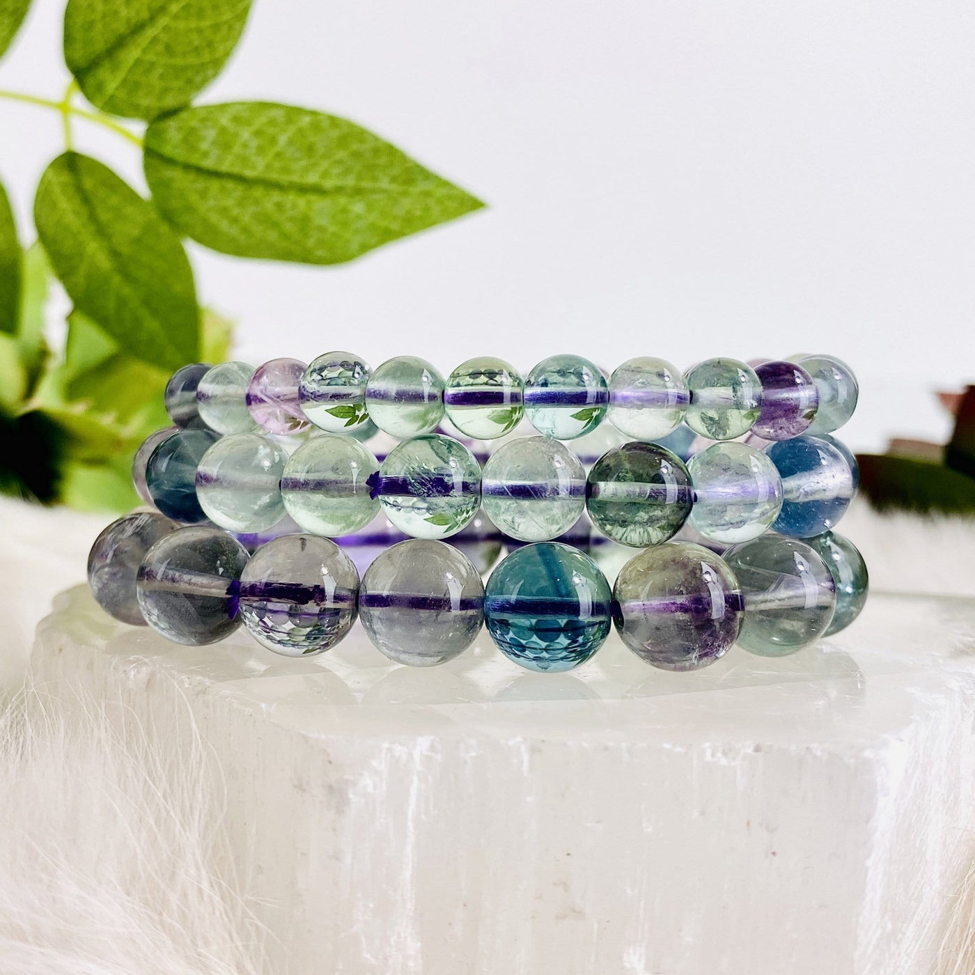 3 Rainbow Fluorite Round Bead Bracelets stacked on top of crystal quartz slab with white background