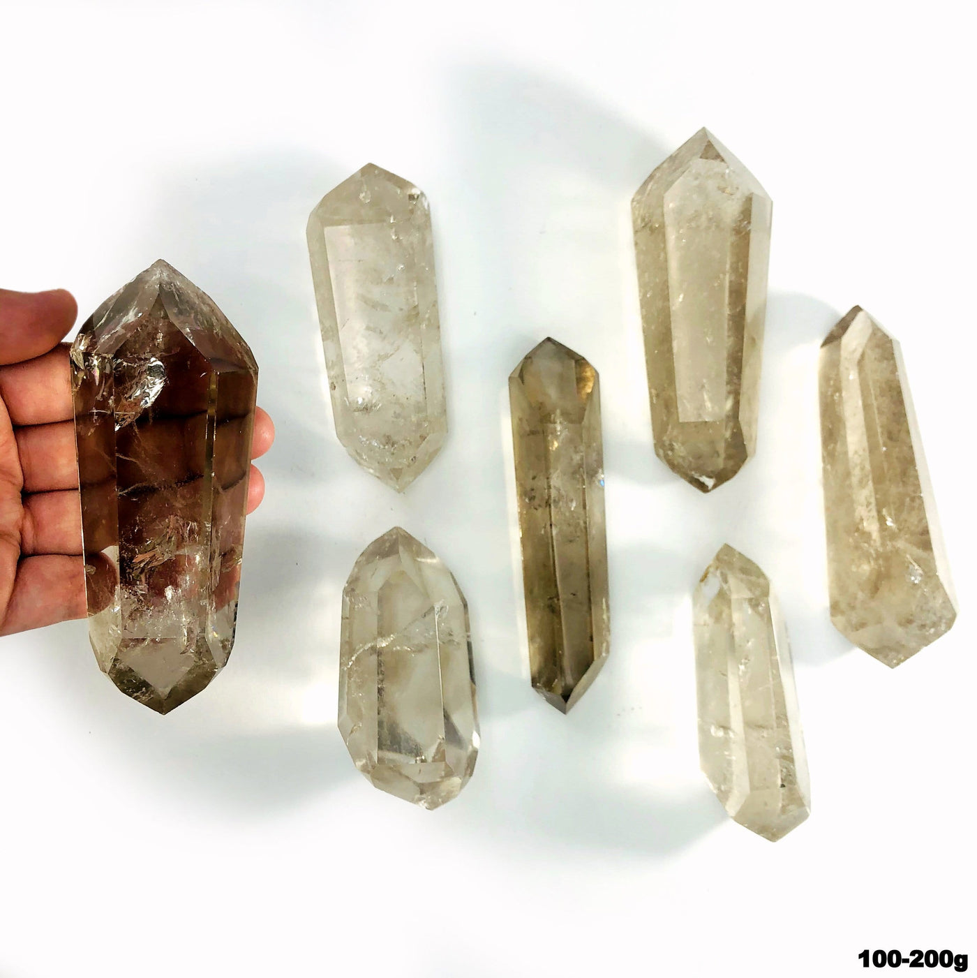 overhead view of many 100g - 200g  smokey quartz double points on white backdrop with one in hand for size reference