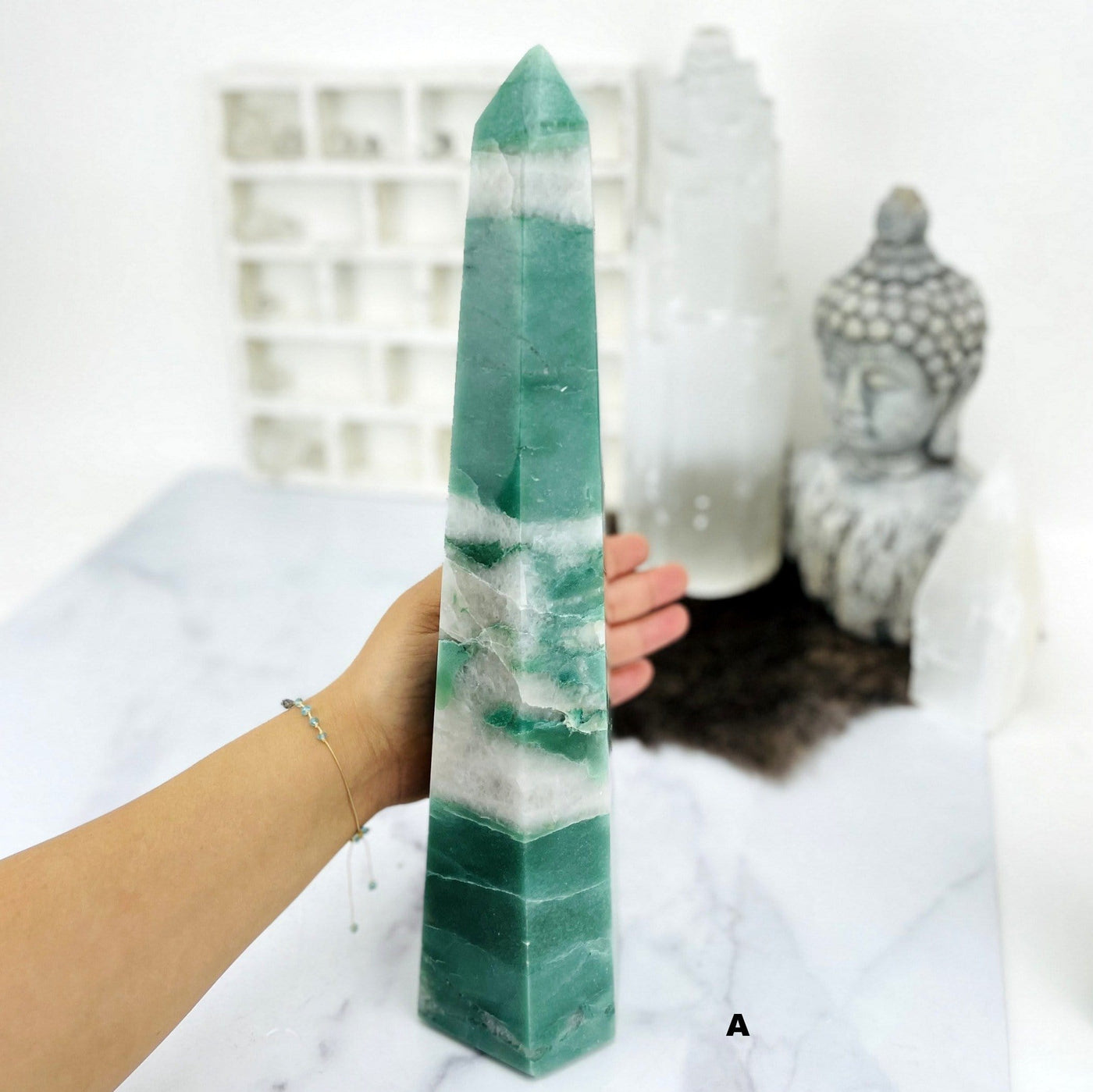 hand behind Green and White Quartz Polished Point with decoration blurred in the background