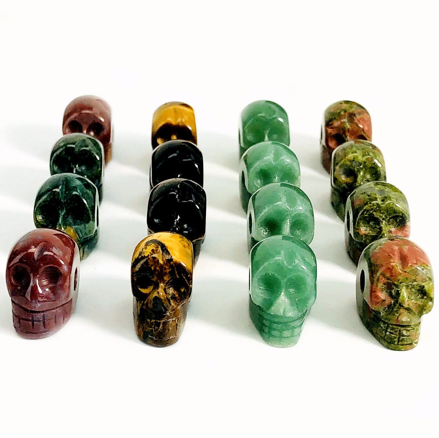 bloodstone, tigers eye, aventurine, and unakite skull beads in rows on white background