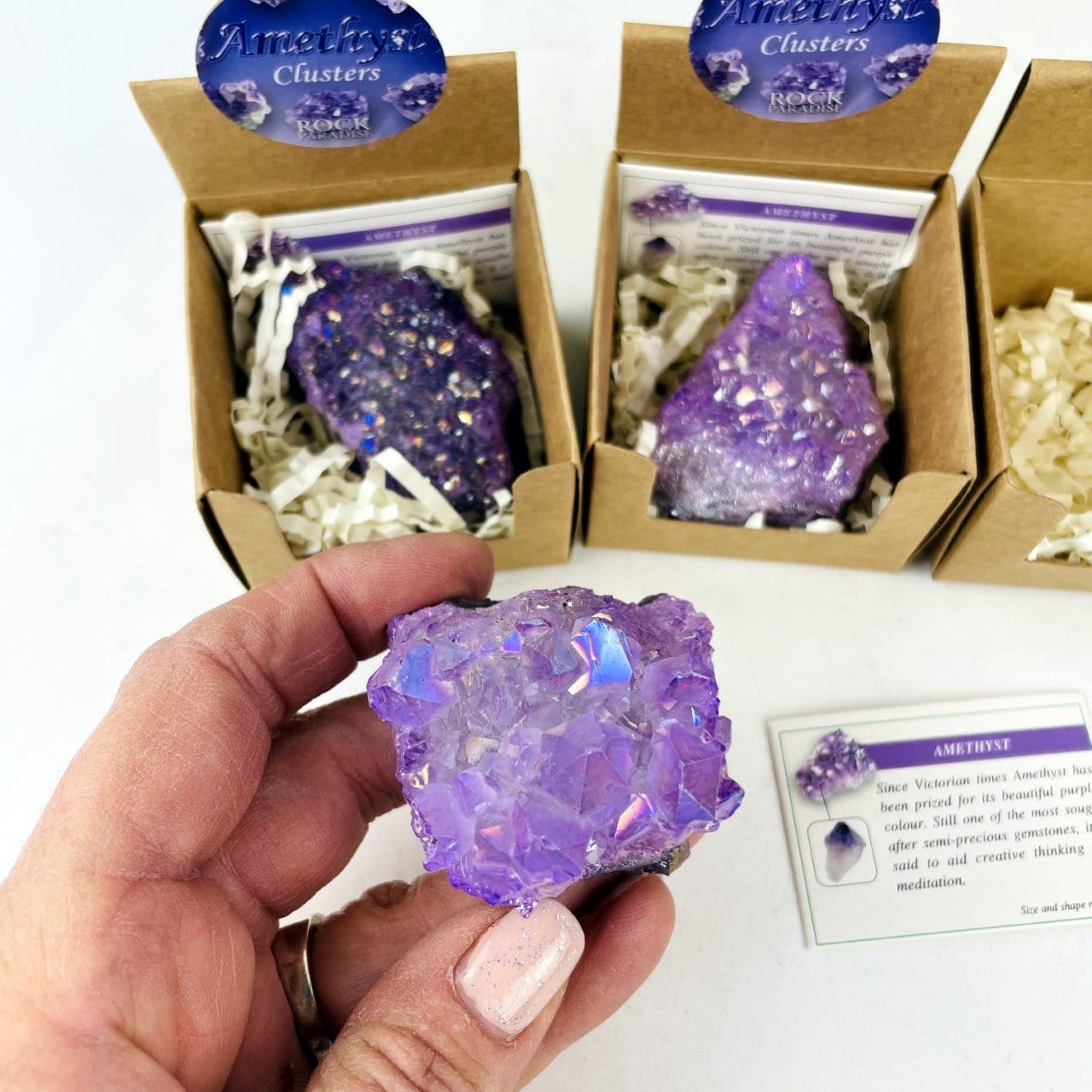 hand holding up amethyst aura geode in box with decorations in the background