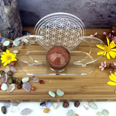 Acrylic Sphere Holder - Crescent Moons with Flower of Life displayed from above in an alter holding a sphere. Flowers and crystals are surrounding the holder.