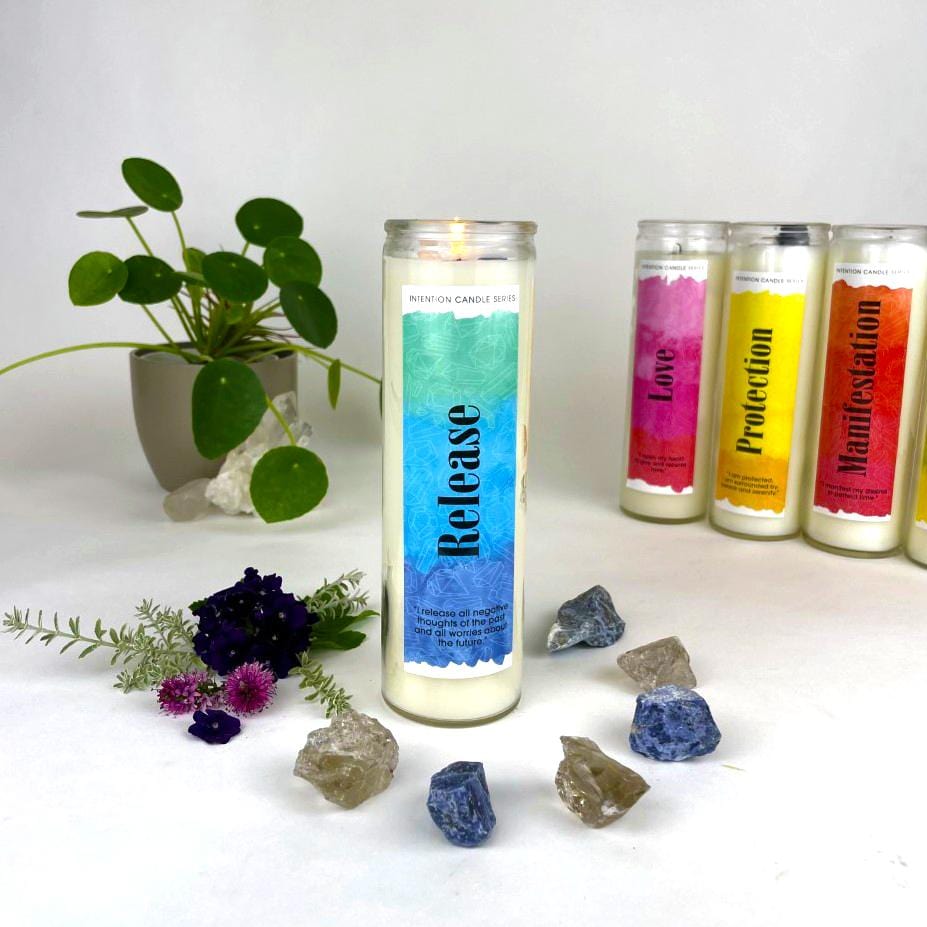 Release Intention Candle surrounded with crystals and flowers with other candles and a plant in the background