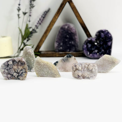 6 different hand holding up variant 2 of Amethyst Flower Crystal Clusters with decorations in the background