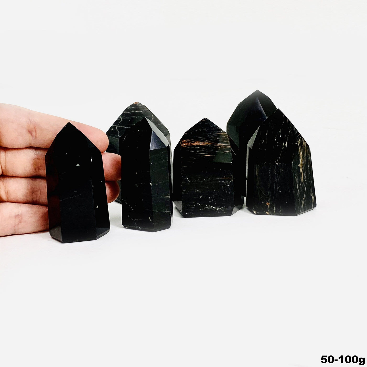 hand behind 50-100g black tourmaline with red iron polished points