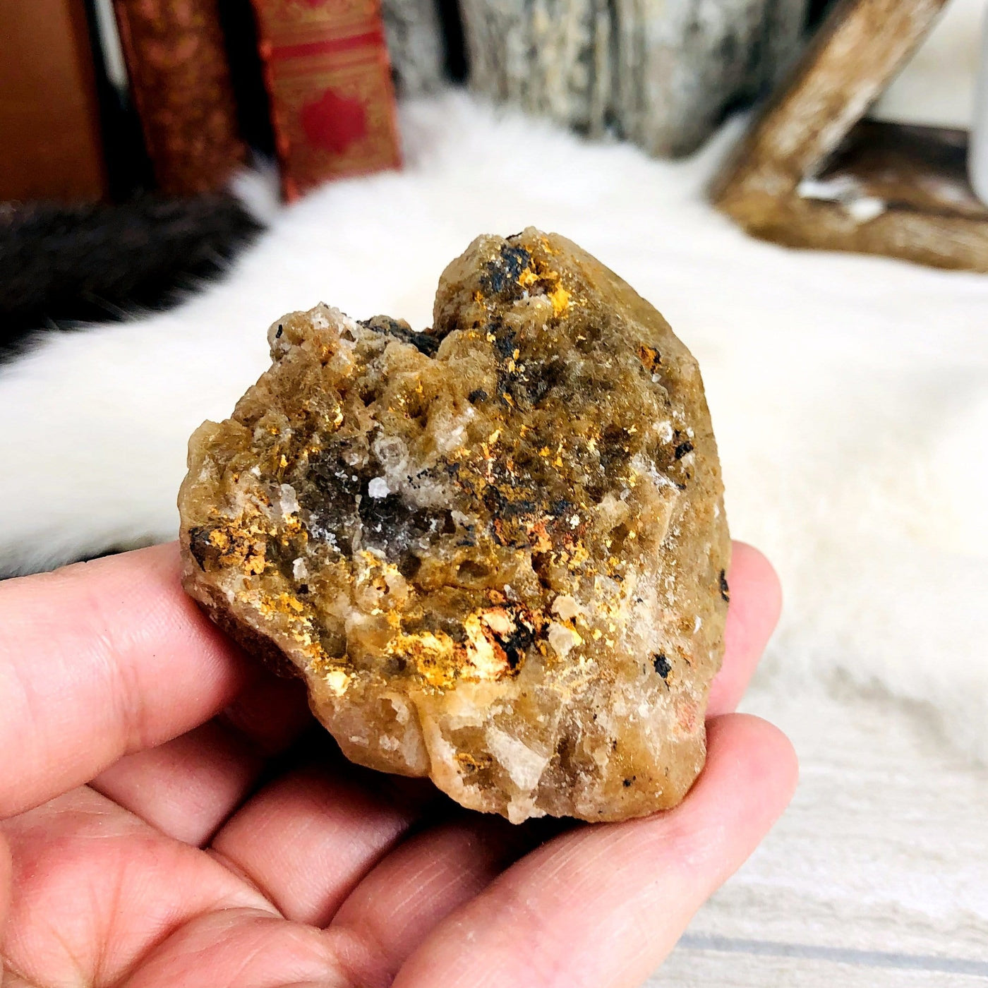 hand holding up Rutilated Natural Smokey Quartz Raw Formation with decorations in the background