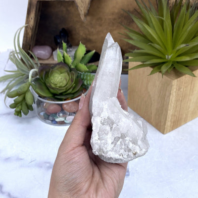 hand holding up Crystal Quartz Cluster with decorations in the background