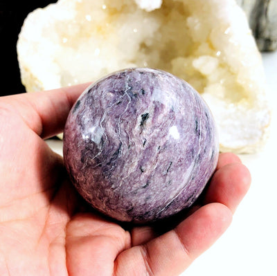 hand holding up Charoite Polished Sphere with decorations in the background