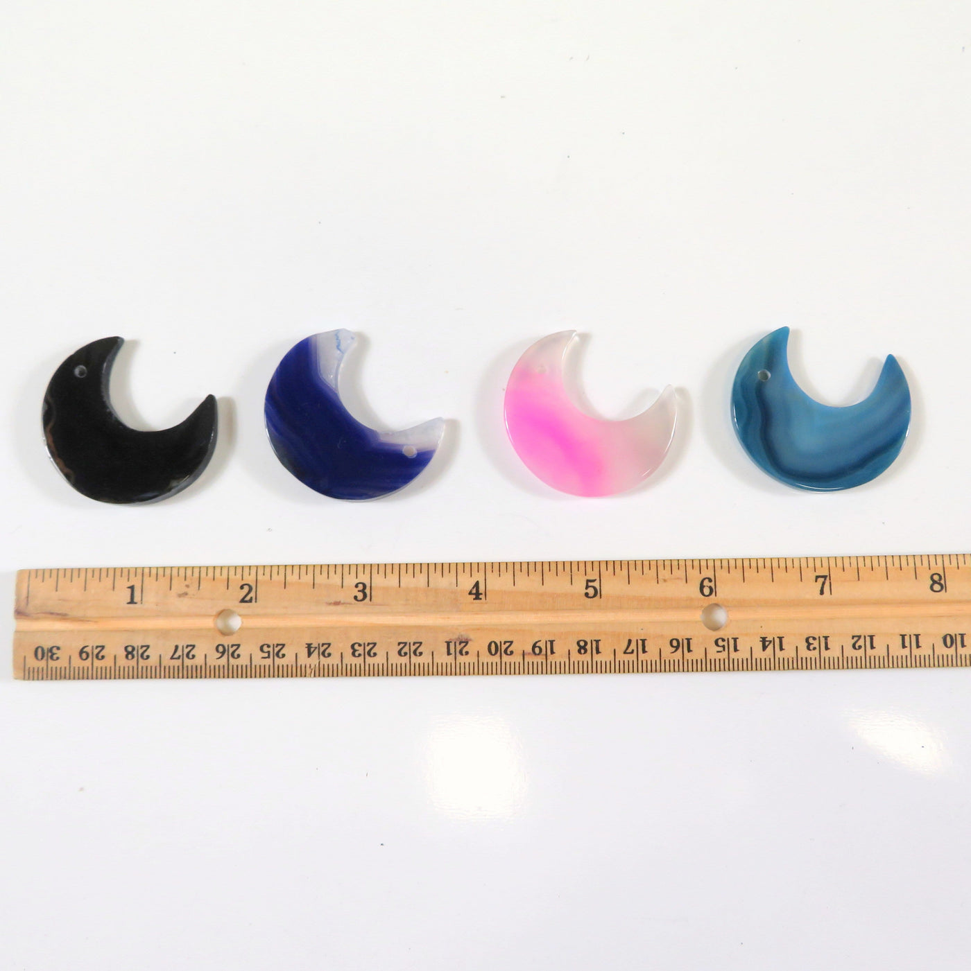 4 Different Color Drilled Agate Moons Under them a Ruler Showing The Size on White Background.