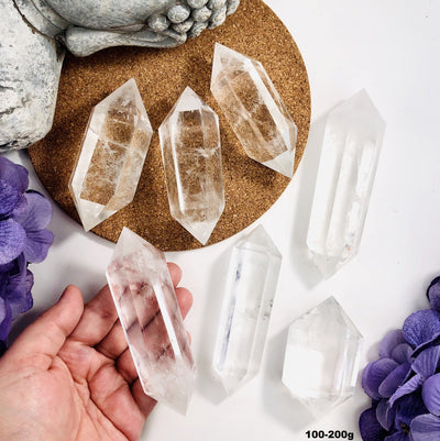 Crystal Quartz Double Terminated Points on a table with some in a hand for size reference - 100-200g