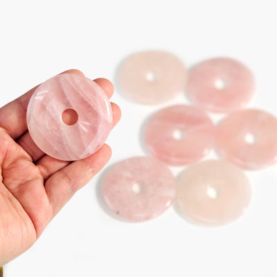hand holding up rose quartz donut shaped polished stone with others blurred in the background