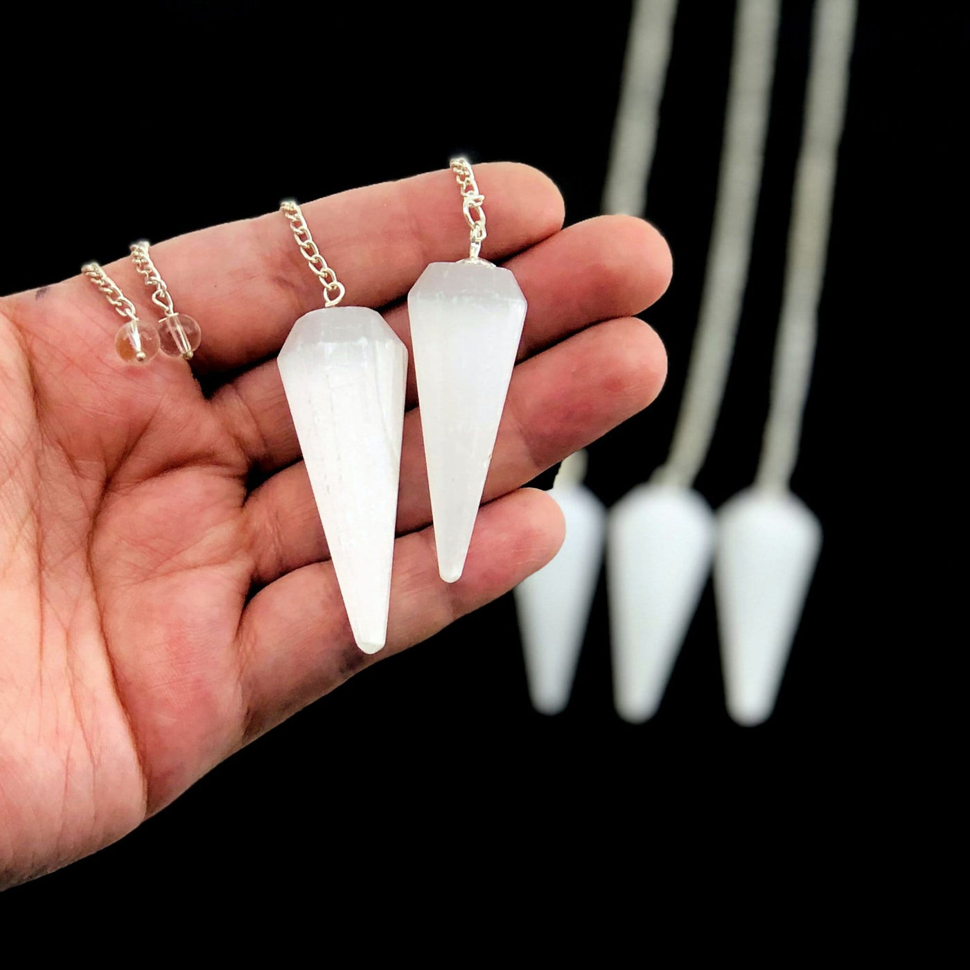 hand holding up 2 selenite point pendulums with others in the background