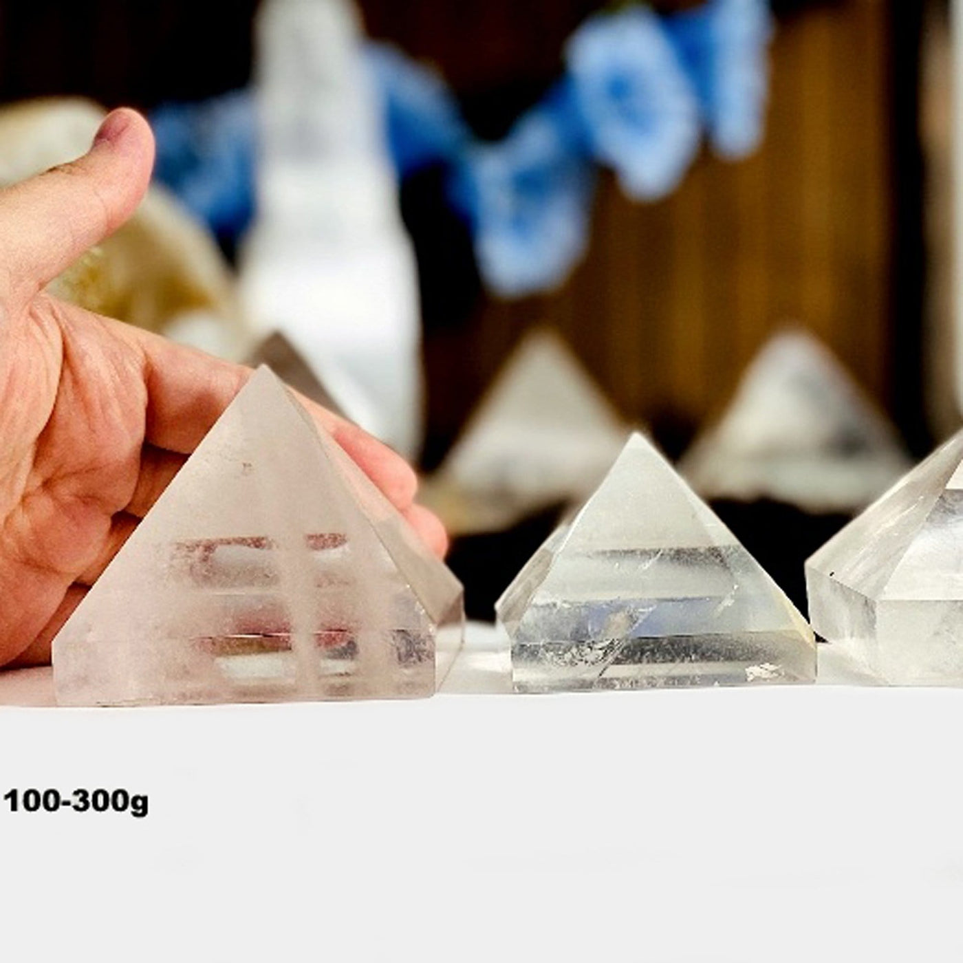 hand behind 100-300g Crystal Quartz Pyramid with others in the background