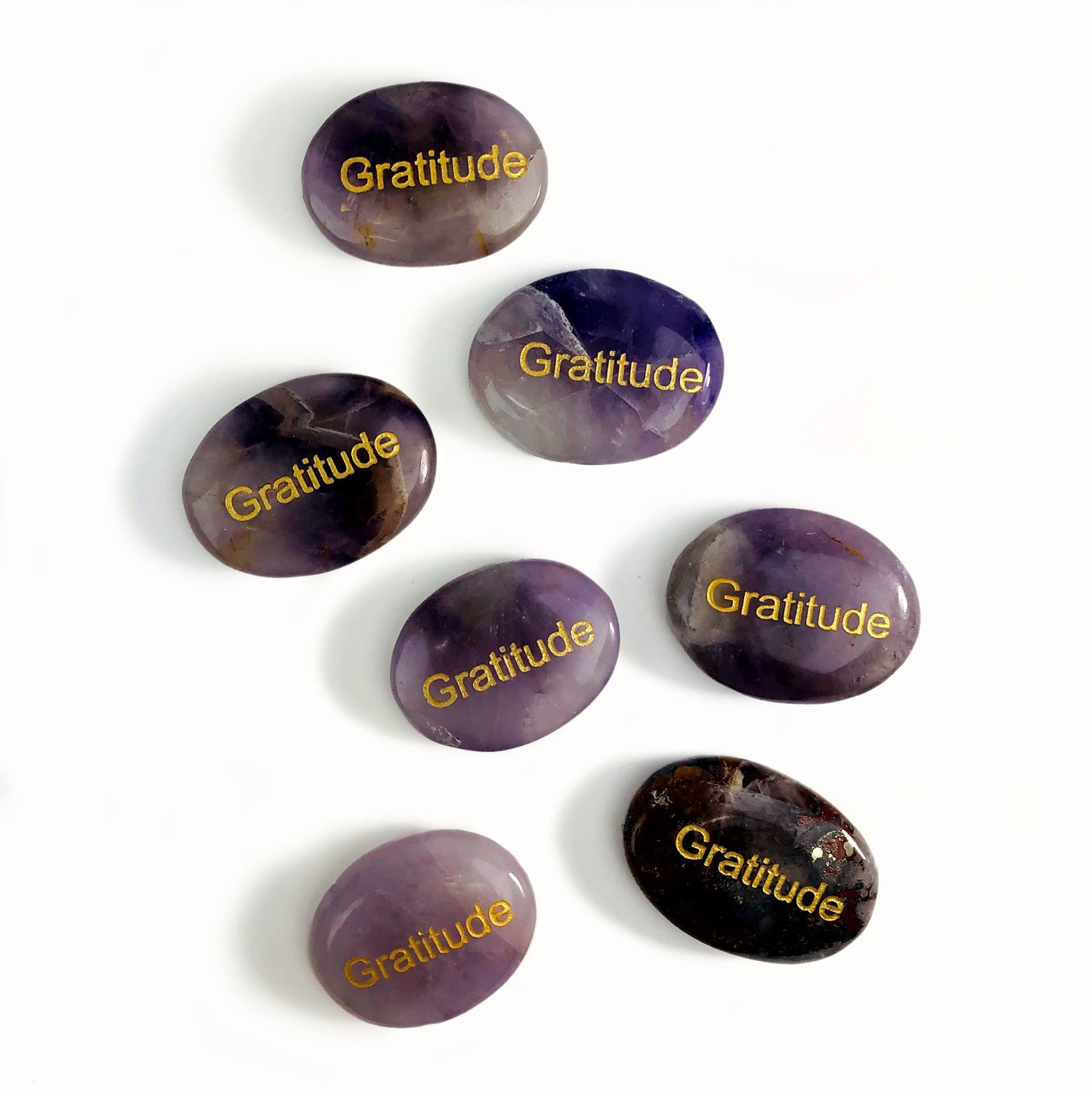 Seven Amethyst "Gratitude" Pocket Palm Stones laid out on a white surface.