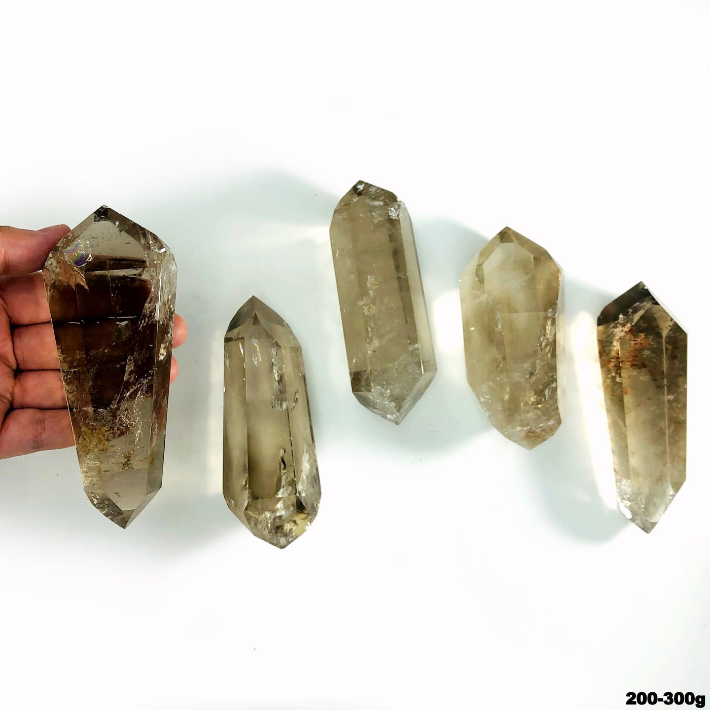 overhead view of many 200g - 300g  smokey quartz double points on white backdrop with one in hand for size reference