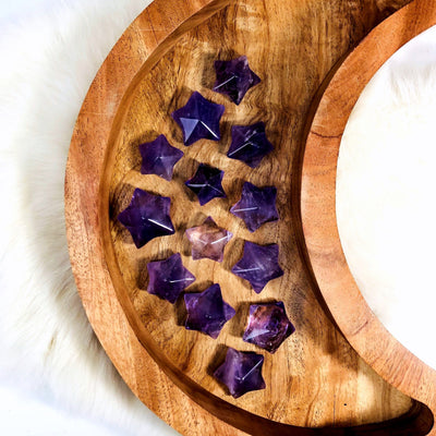 13 Amethyst Puffy Star Cabochon Gemstones displayed on a wooden moon shaped tray.