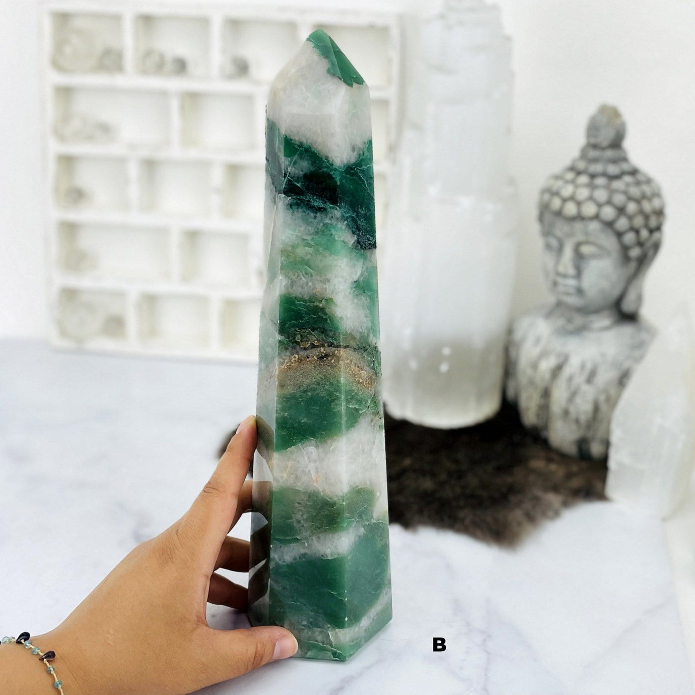 hand next to Green and White Quartz Polished Point with decorations in the background