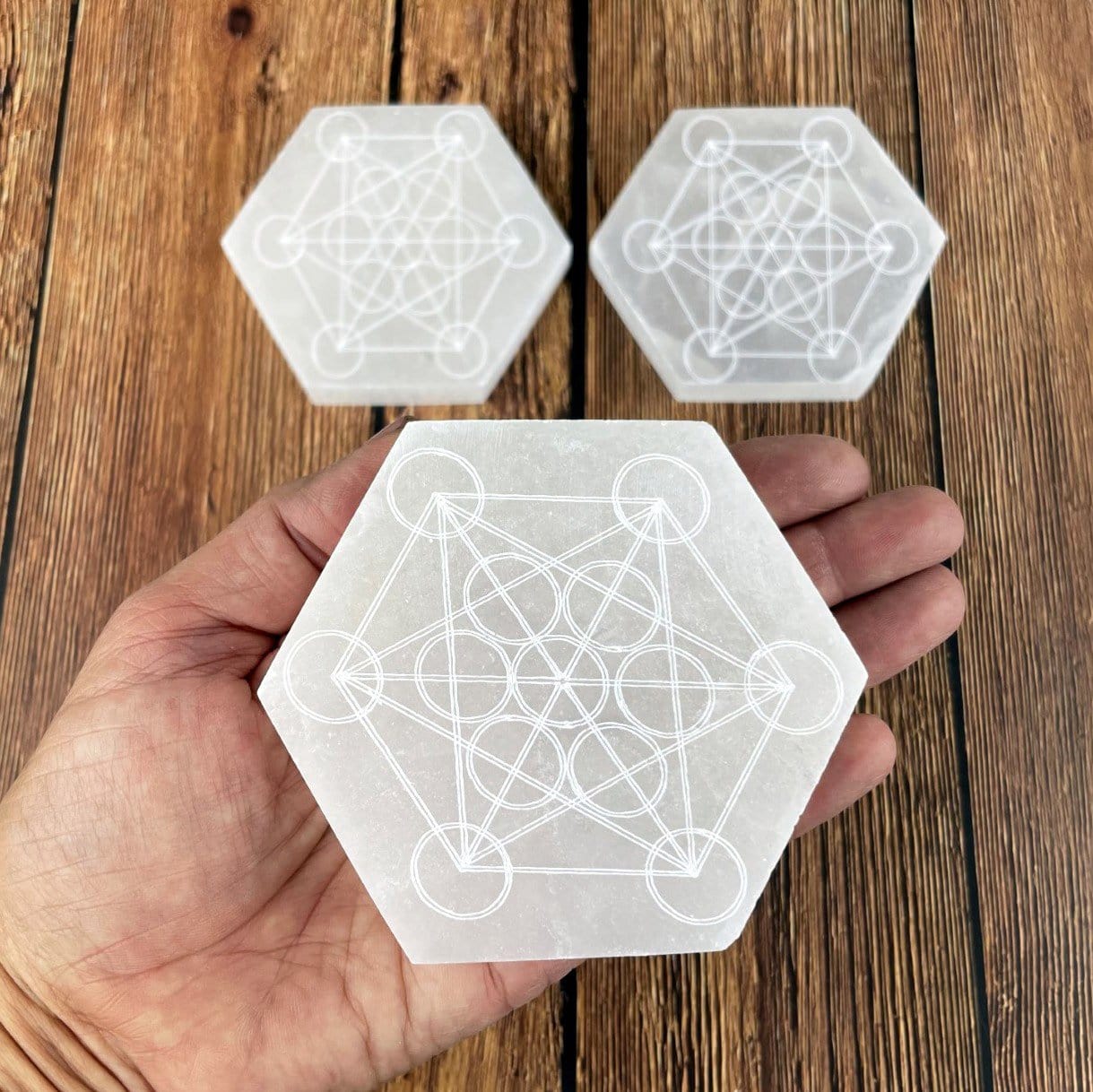 selenite hexagon engraved with metatron symbol in hand for size reference with others in background