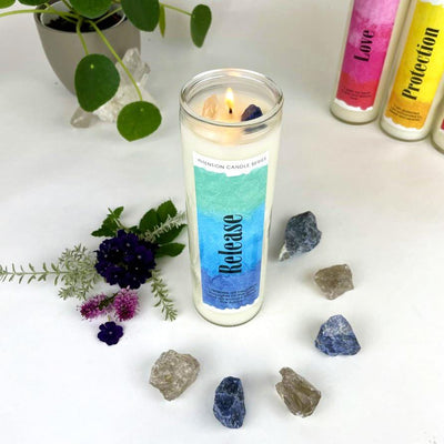 Release Intention Candle surrounded by crystals and flowers with a plant and other candles in the background