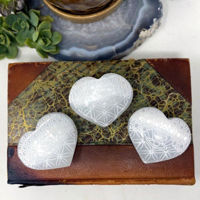 overhead view of three selenite stone hearts with eye engraving on display for engraving details