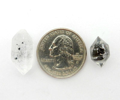 Assorted tibetan crystal quartz double terminated on a white background next to a quarter.