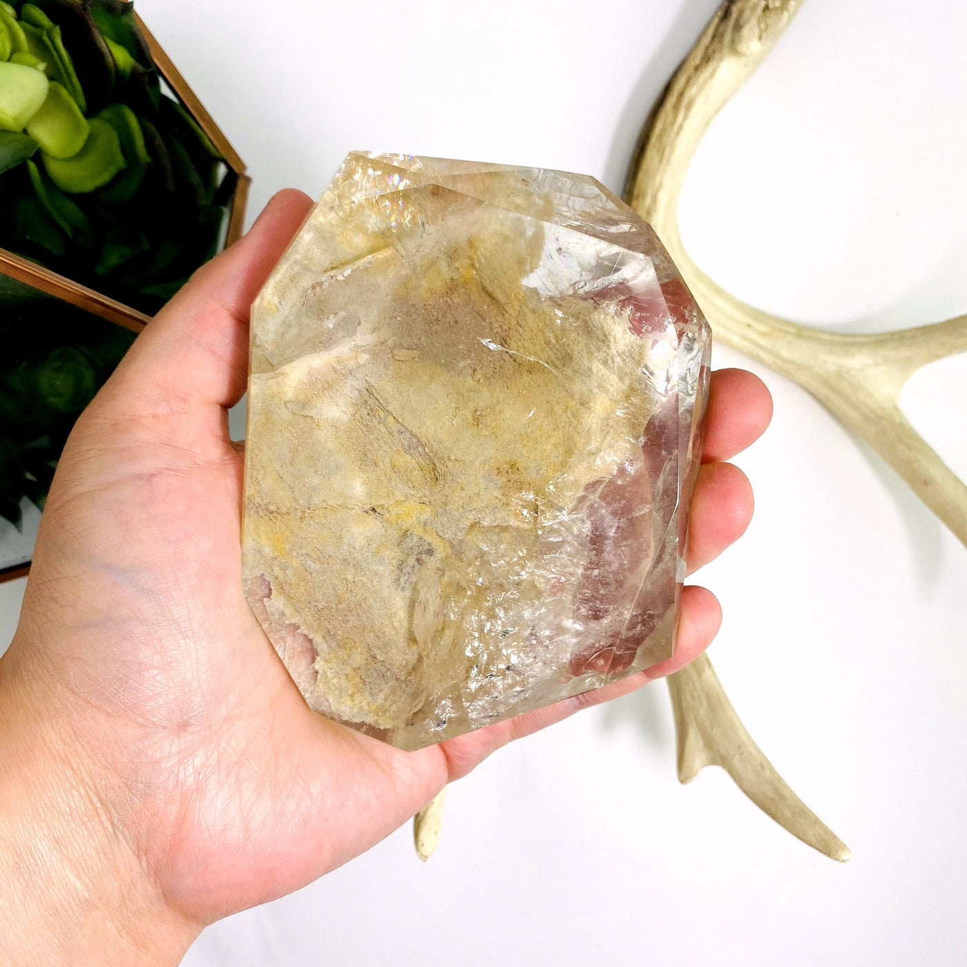 hand holding up Crystal Quartz Polished Stone with decorations in the background