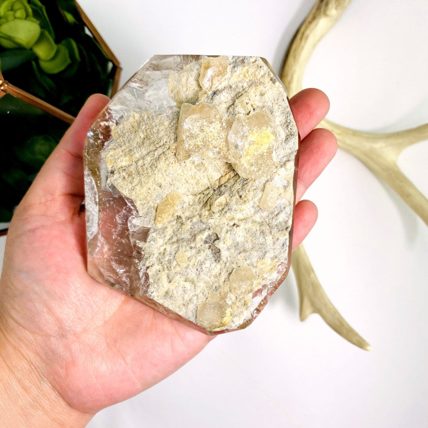 hand holding up Crystal Quartz Polished Stone with decorations in the background
