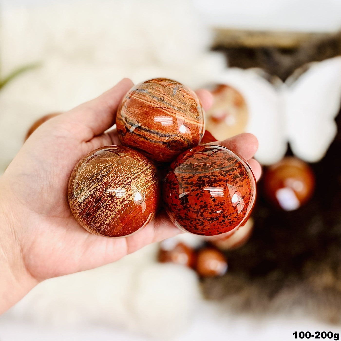 Hand holding up 3 100-200g Red Jasper Polished Spheres with decorations blurred in the background
