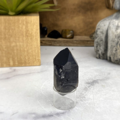 close up of dark smokey quartz on clear stand in front of backdrop for details