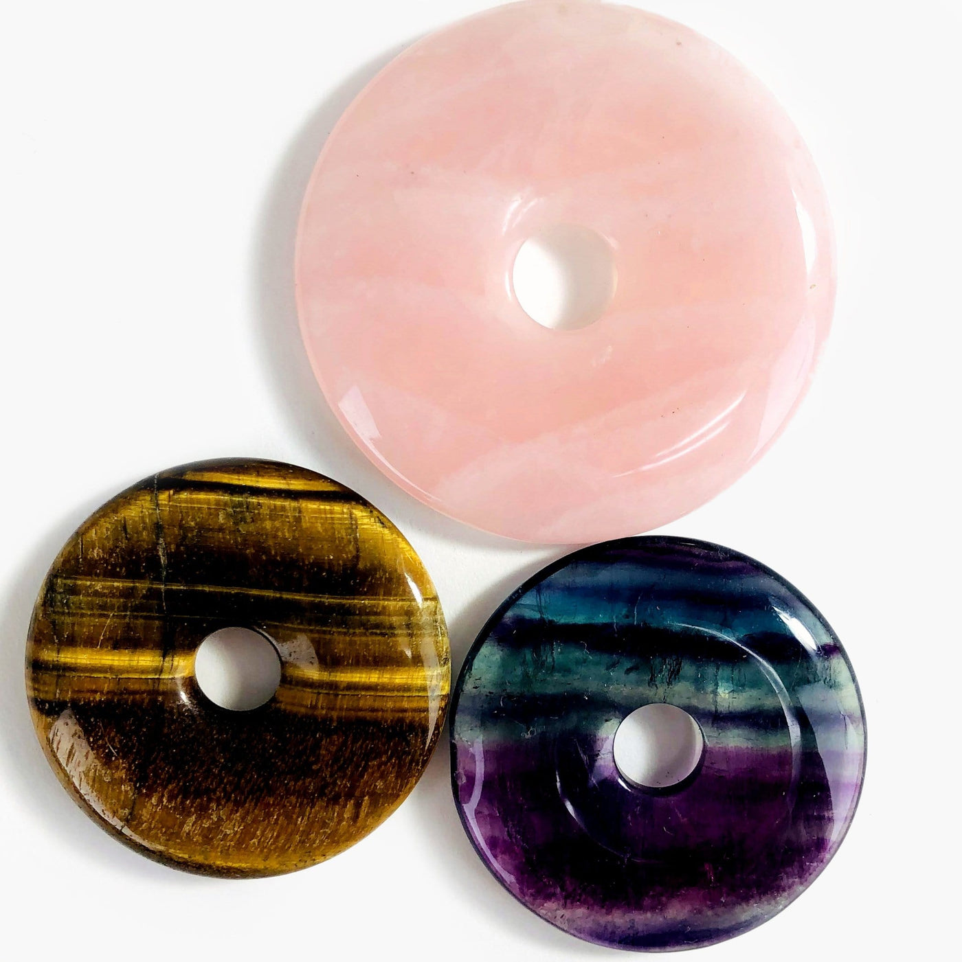 rose quartz, tigers eye, and fluorite donut shaped polished stones on white background