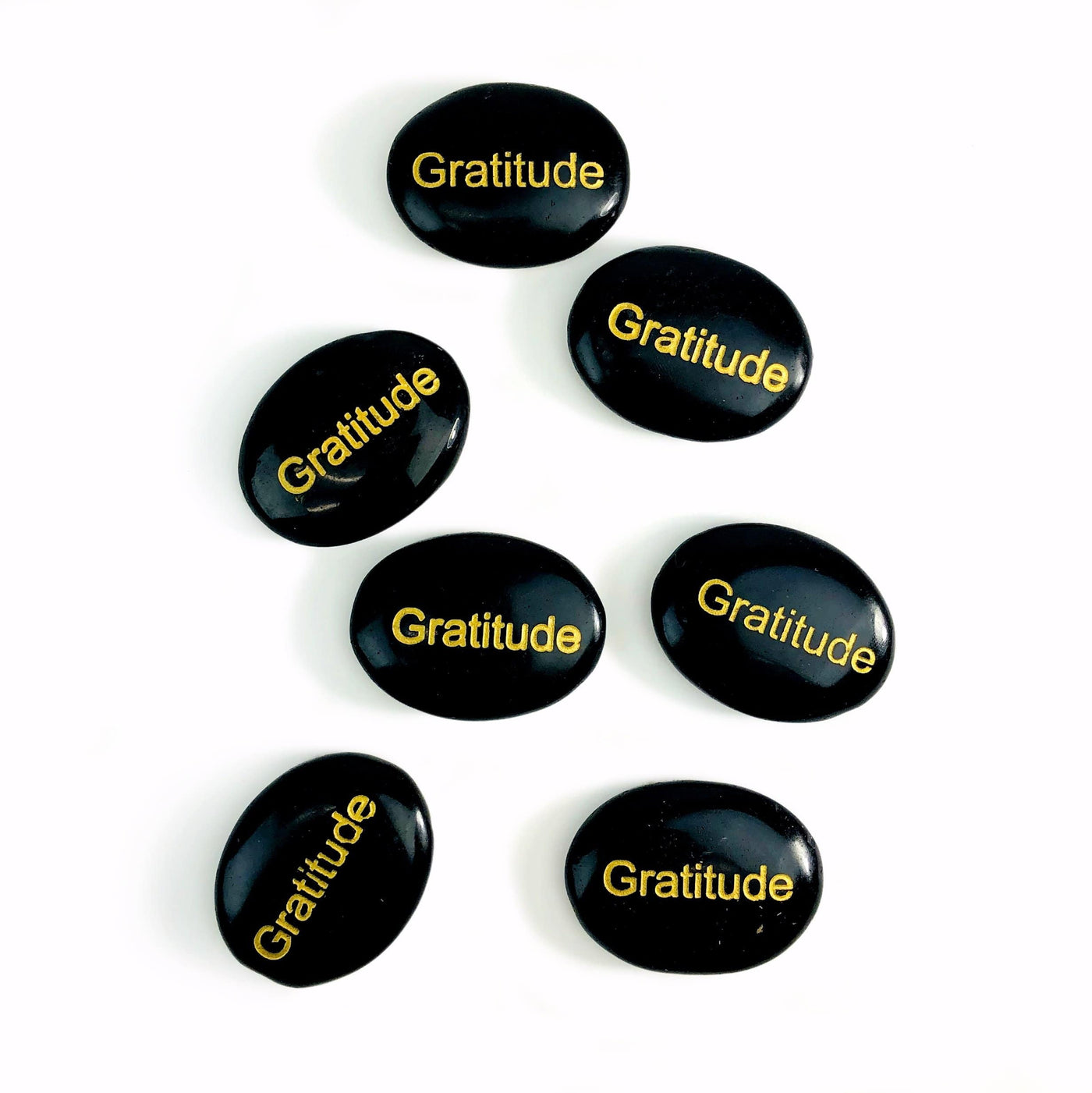 Seven Black Obsidian "Gratitude" Pocket Palm Stones laid out on a white surface.