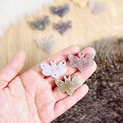 hand holding up 3 druzy bumblebees with decorations blurred in the background