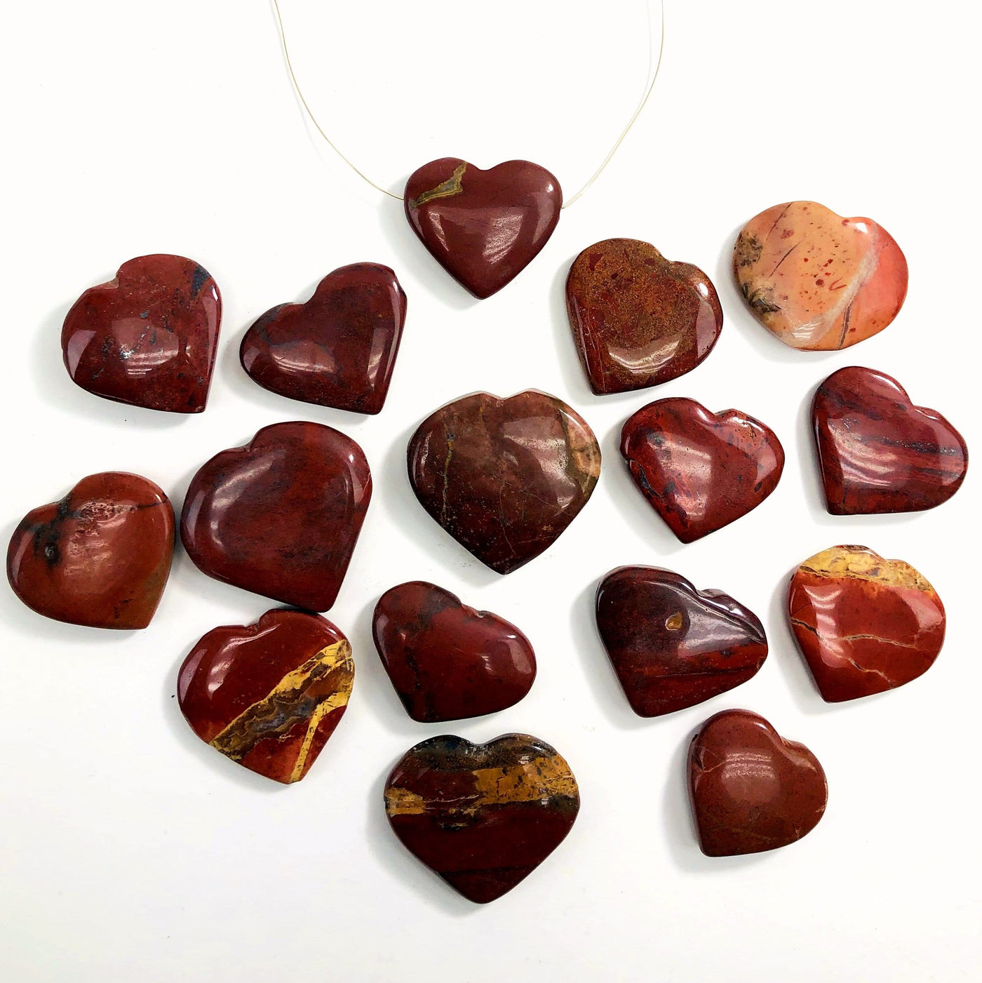 multiple red jasper head drilled heart shaped gemstones in a row one with a wire shown as a neckless