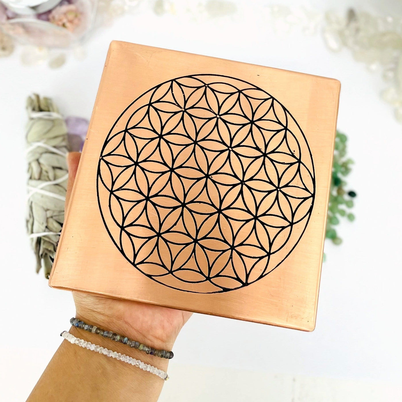 copper square flat plate with a flower of life grid in black on it held in a woman's hand