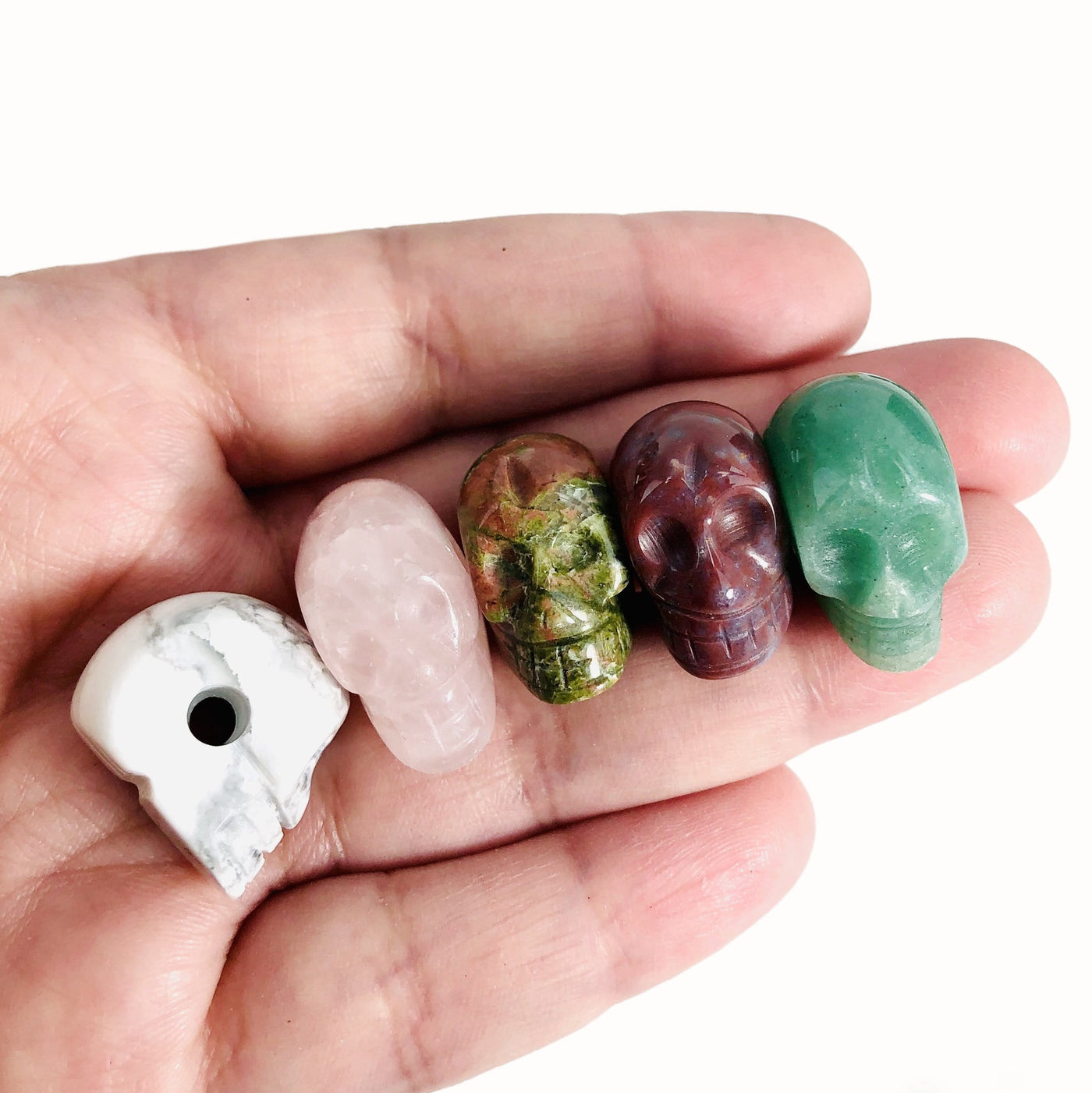 five gemstone skull beads in hand for size reference with one turned sideways to see the drill hole