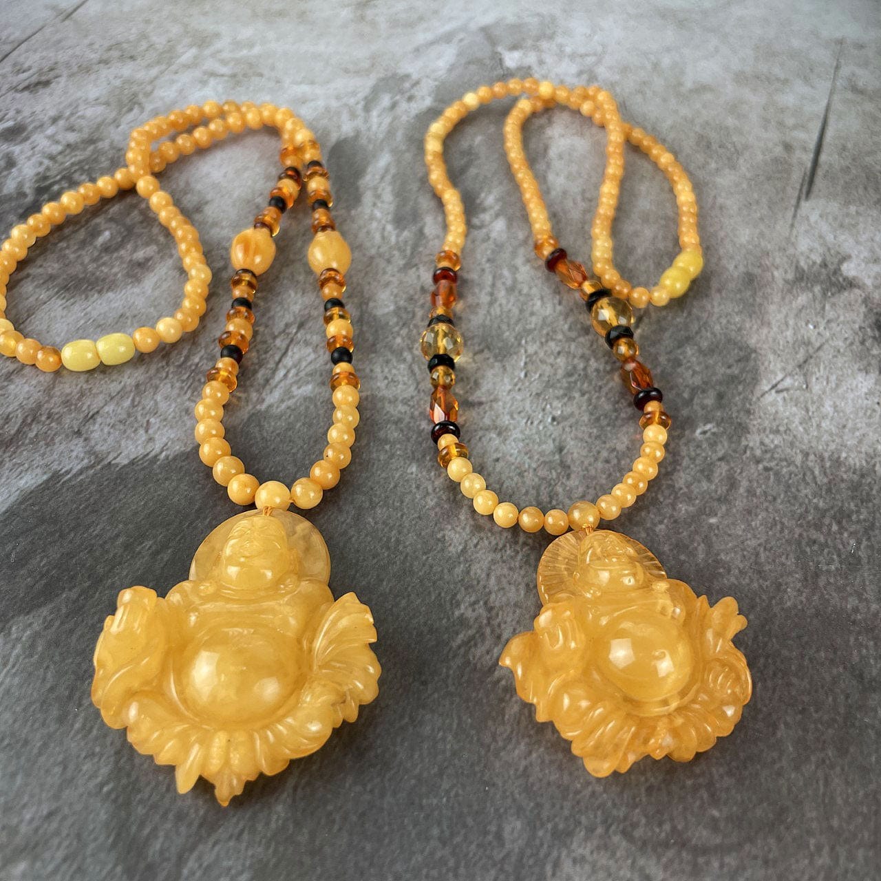 Amber Beaded Necklaces with Carved Buddha Pendants side by side at an agle to show details of the pendants