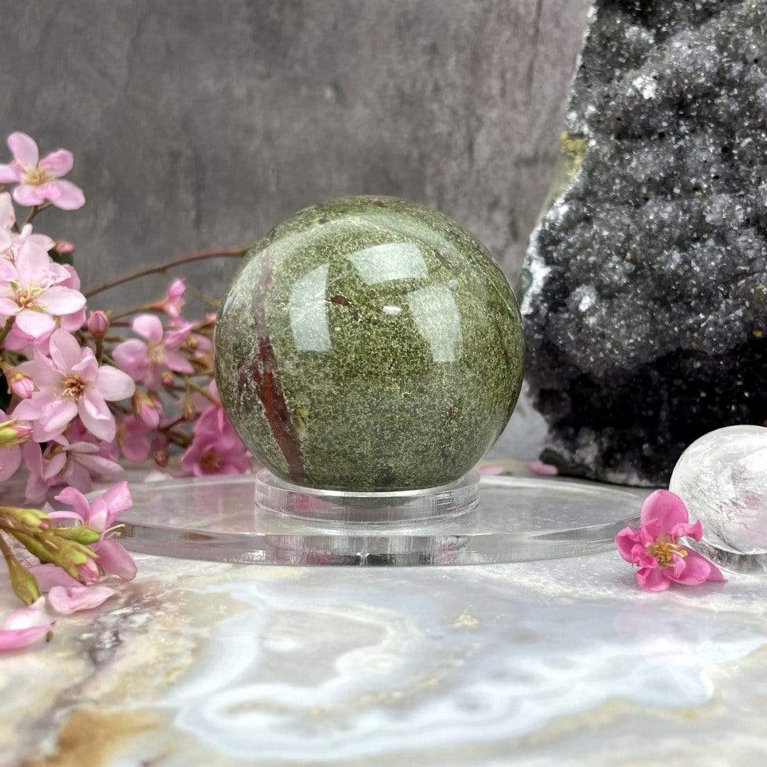 Acrylic Sphere Holder - Clear Oval Holder in an alter decorated with crystals and flowers shown close up at angle holding a sphere.