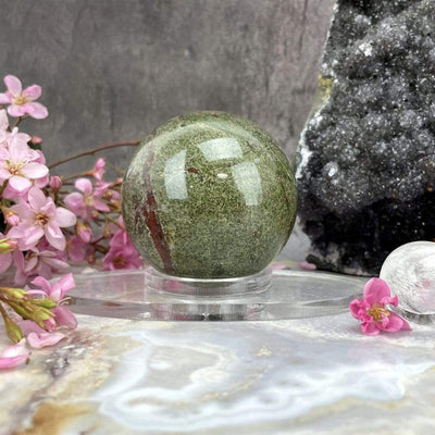 Acrylic Sphere Holder - Clear Oval Holder in an alter decorated with crystals and flowers shown close up at angle holding a sphere.