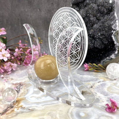 Shown at an angle - Acrylic Sphere Holder Crescent Moons - Flower of Life holding a sphere in an alter that consists of crystals and flowers.